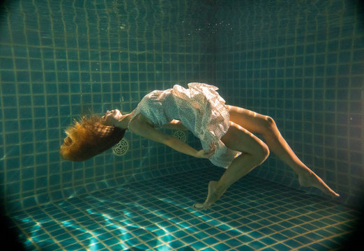 Beautiful woman with long red hair posing underwater in white dress