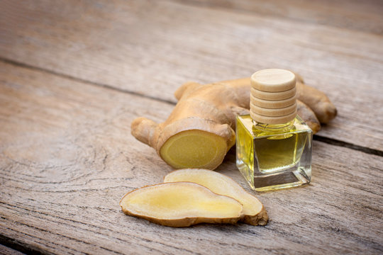 bottle of essential ginger oil with fresh ginger rhizome isolated onc wood table background. 