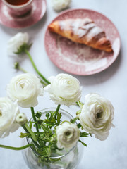 White ranunculus flowers and a cup of tea with croissant blurred in the background