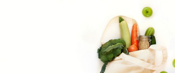 Reusable textile cotton bag with a set of products, vegetables for a healthy balanced diet on white background. Zero waste banner, storage and recycling, eco friendly lifestyle. Top view,copy space.