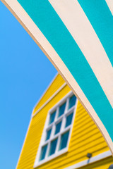 A green blue striped awning with yellow house and blue sky background