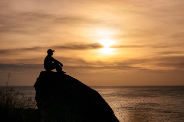 Man sitting on big rock with sightseeing of sunset in tropical sea