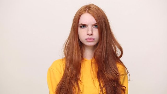 Ginger young secret girl in yellow streetwear hoodie isolated on white background in studio. People emotions lifestyle concept. Looking at camera saying hush be quiet with finger on lips shhh gesture