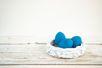 Easter card. Three eggs painted in classic blue color in a white wicker basket on a wooden white table. Copy space for text.