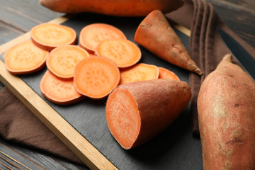 Sweet potato, knife, board and towel on wooden background, close up