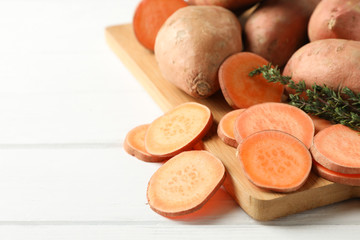 Sweet potato, thyme and board on white wooden background, close up