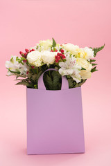 bouquet of flowers in violet paper bag on pink background