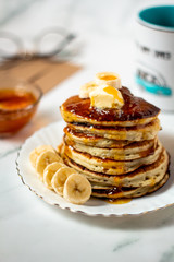 Hot tasty american pancakes. Blue and brown background. Served with bananas and melted butter on the white table. Mug, glasses, daily planner and envelope background. Vertical orientation