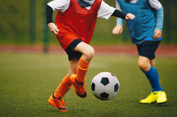 Junior youth soccer team compete on grass pitch. Soccer summer school tournament. Running soccer players in duel. Youth athletes kicking black and white football ball