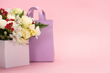 bouquet of flowers in festive gift box near violet paper bag on pink background