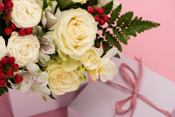 close up view of bouquet of flowers in festive gift box with bow on pink background