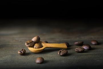 Roasted coffee beans lie in a small spoon on a dark wooden rustic table. Focus concept.