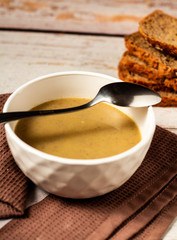 Hot tasty mushroom cream soup in a white bowl on a brown kitchen towel with bread background and tablespoon above
