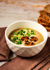 Hot tasty mushroom cream soup decorated with green onion and fried mushrooms in a white bowl on a brown kitchen towel with bread background. Negative space