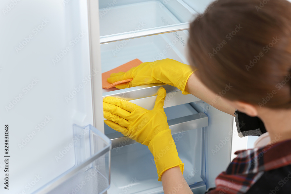 Wall mural Woman in rubber gloves cleaning refrigerator, closeup