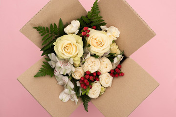 top view of bouquet of flowers in cardboard box on pink background