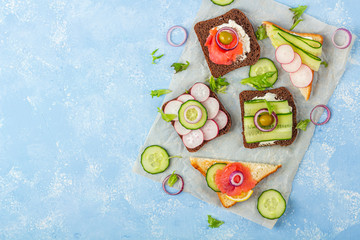 Appetizer, open sandwich with different toppings: salmon and vegetables on a paper on blue background. Traditional Italian or Scandinavian snack. Healthy eating. Close up, copy space for text
