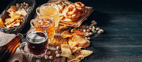three glasses of expensive craft beer, classic and unfiltered and dark in a glass on the table with a snack of peanut and pistachio chips and nachos