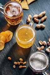 three glasses of expensive craft beer, classic and unfiltered and dark in a glass on the table with a snack of peanut and pistachio chips and nachos