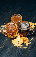 three glasses of expensive craft beer, classic and unfiltered and dark in a glass on the table with a snack of peanut and pistachio chips and nachos