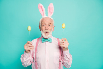 Portrait of astonished grandfather man celebrate easter party hold colorful eggs stick he get from his grand kids impressed scream wow omg wear pink shirt isolated teal color background