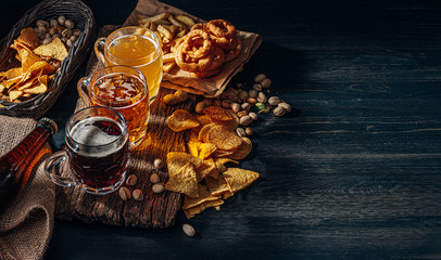 three glasses of expensive craft beer, classic and unfiltered and dark in a glass on the table with a snack of peanut and pistachio chips and nachos