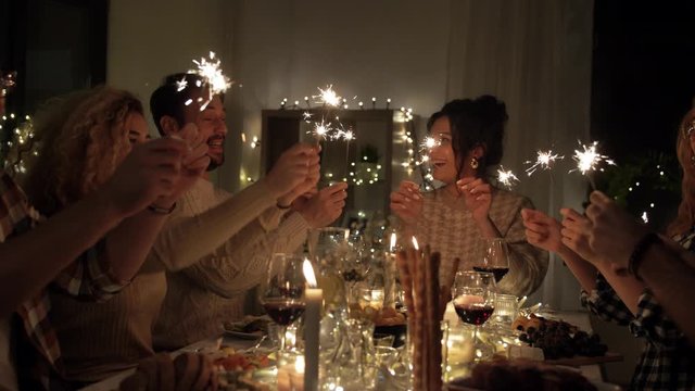 holidays, celebration and people concept - happy friends with sparklers having christmas dinner at home