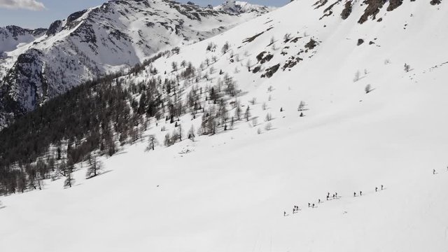 winter aerial over group of people with snowshoes hiking down a snowy slope. Winter wonderland panorama with active people.Mountains outdoor establisher.4k drone circle pan flight