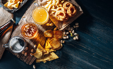 three glasses of expensive craft beer, classic and unfiltered and dark in a glass on the table with a snack of peanut and pistachio chips and nachos