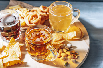 three glasses of expensive craft beer, classic and unfiltered and dark in a glass on the table with a snack of peanut and pistachio chips and nachos