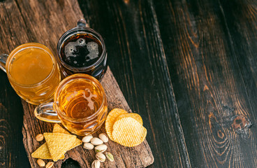 three glasses of expensive craft beer, classic and unfiltered and dark in a glass on the table with a snack of peanut and pistachio chips and nachos