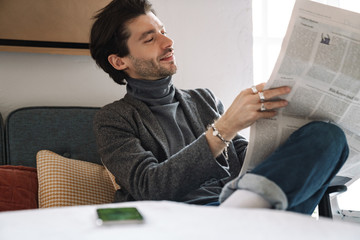 Image of young businessman sitting at table and reading newspaper in cafe