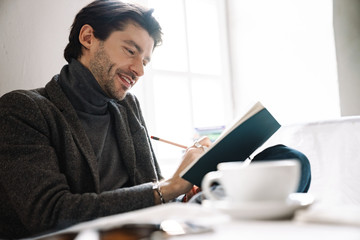 Image of caucasian man taking notes and talking on cellphone in cafe