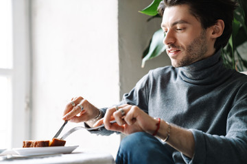 Obraz na płótnie Canvas Image of handsome man eating dessert while having breakfast in cafe