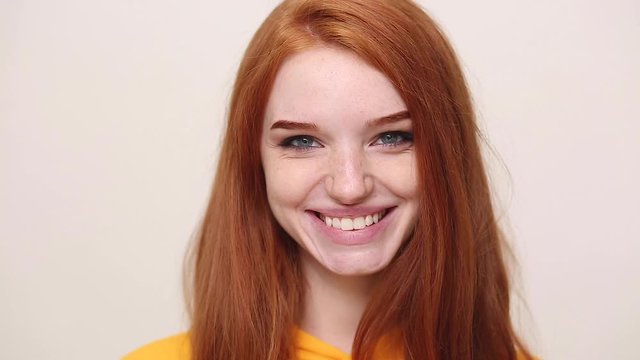 Close up happy charming ginger redhead curly young girl in yellow streetwear hoodie posing isolated on white background in studio. People sincere emotions lifestyle concept. Looking at camera smiling