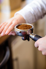 Hand of barista holding coffee machine holder filled with coffee