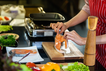 Hand of woman and pepper bottles made of wood cooking delicious salmon steak at the kitchen.