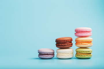 Macaroni cookies of different colors are arranged in the shape of pyramid steps on a blue background.