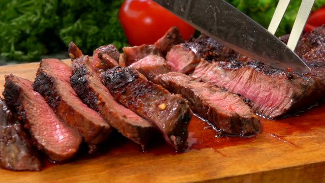 Panorama movement along the prepared juicy beef steak cut on slices with a knife on a wooden board