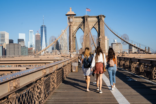 Fototapeta Three girls walking on the Brooklyn Bridge with the New York skyline on the back