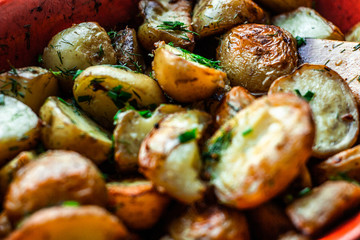 Tasty baked potato wedge on a wooden spatula, baked with spices, chopped garlic, olive oil and fresh chopped dill and green onion in a baking dish. Top view. Horizontal orientation