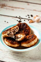 Belyashi or tasty homemade fried dough with minced meat. Pies are on a white and blue plate on a wooden table. Black peppercorns and garlic background. Side view. Copy space. Vertical orientation