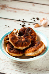 Belyashi or tasty homemade fried dough with minced meat. Pies are on a white and blue plate on a wooden table. Black peppercorns and garlic background. Copy space. Vertical orientation