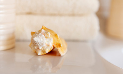 Сockleshell and Bath white cotton towels, ceramic bottle on Blurred bathroom interior background with sink and faucet.