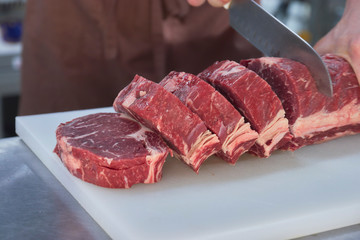 Butcher cutting beef in the kitchen. Closeup of hands with a knife and meat.