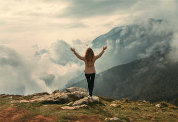 Tourist Woman standing on top mountain turned away raised arms enjoy divine view mountains in white...