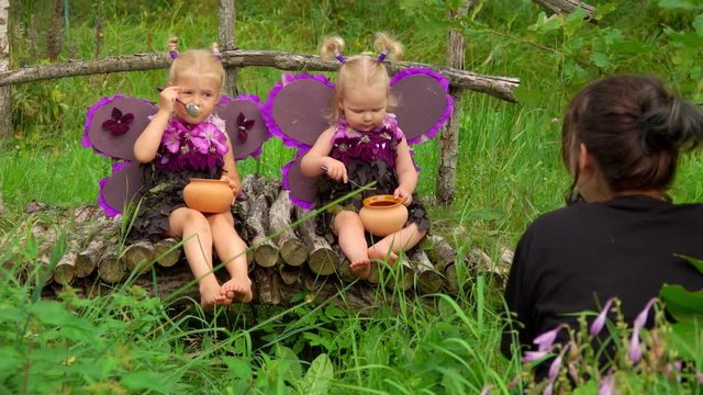Female photographer takes pictures of beautiful girls playing violet butterflies. Girls wear handmade butterfly wings and wave their hands