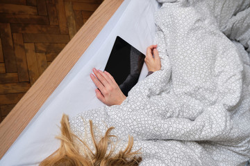 Woman holds tablet in hands. Morning online activities in home. Relax in bed, watching movies and TV shows on mobile device. Social media addiction. Work at home, freelance. Technology in lifestyle