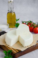 Homemade fresh soft cheese brynza or feta on a wooden cutting board with parsley and cherry tomatoes on a gray background. Vertical orientation.