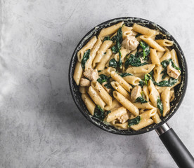 Pasta with chicken spinach and cream in black pan on grey background